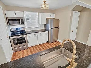 kitchen with sink, stainless steel appliances, white cabinets, and light hardwood / wood-style floors