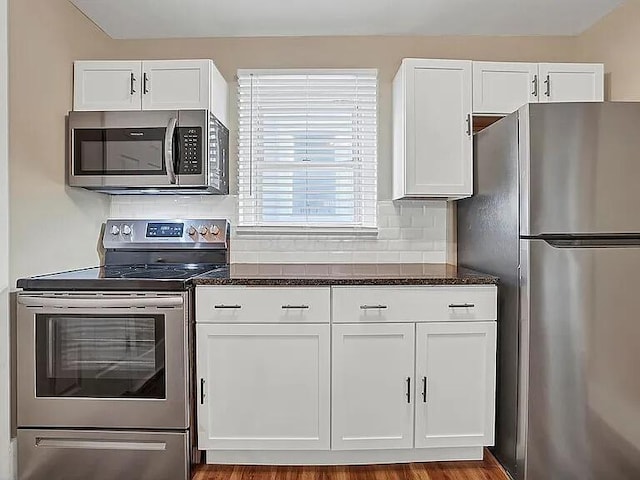 kitchen featuring white cabinets, stainless steel appliances, dark stone countertops, and light hardwood / wood-style floors