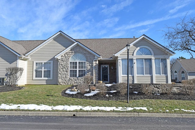 ranch-style home featuring a shingled roof, a front yard, and stone siding