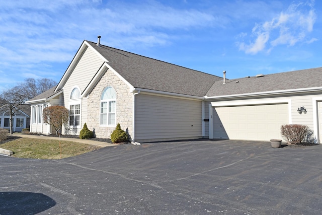 view of side of home with stone siding, a shingled roof, an attached garage, and driveway