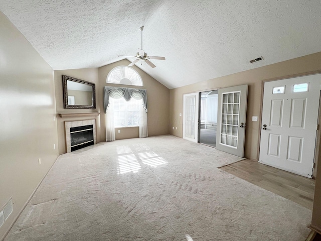 unfurnished living room with a tile fireplace, ceiling fan, a textured ceiling, light carpet, and vaulted ceiling