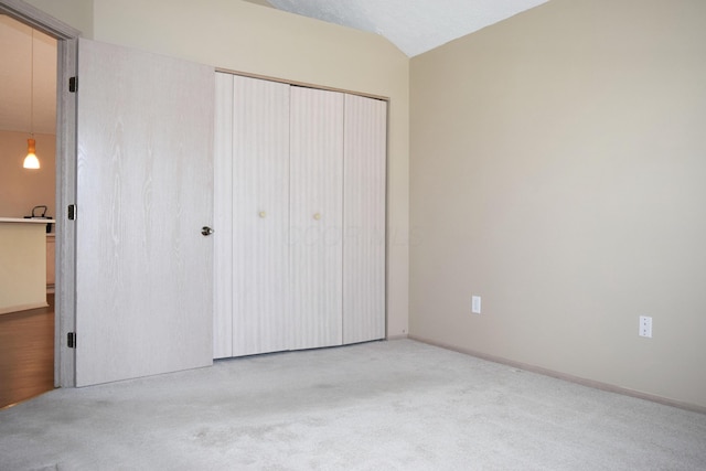 unfurnished bedroom featuring light colored carpet, vaulted ceiling, and a closet