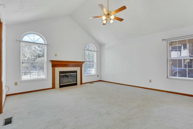 unfurnished living room with a wealth of natural light, light colored carpet, a tile fireplace, and ceiling fan