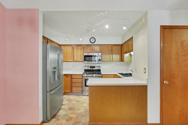 kitchen with sink, tasteful backsplash, track lighting, appliances with stainless steel finishes, and kitchen peninsula