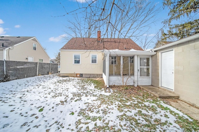 snow covered back of property with a sunroom