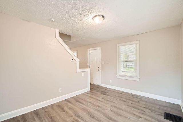 spare room featuring a textured ceiling, wood finished floors, baseboards, and stairs