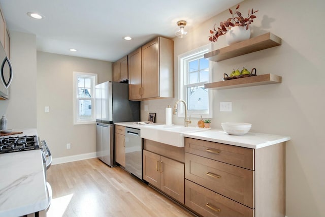 kitchen with stainless steel appliances, light stone countertops, sink, and light hardwood / wood-style flooring