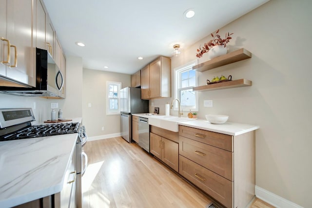 kitchen featuring stainless steel appliances, light stone countertops, sink, and light wood-type flooring