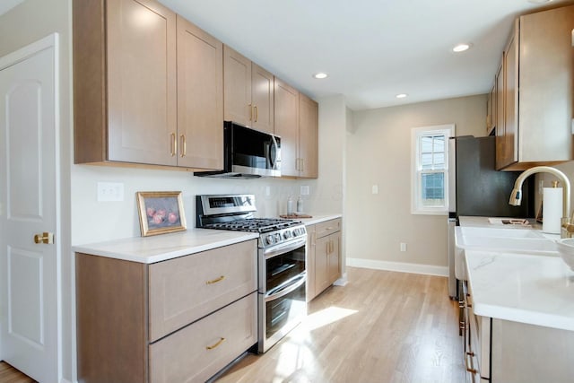 kitchen with stainless steel appliances, sink, light brown cabinets, and light wood-type flooring