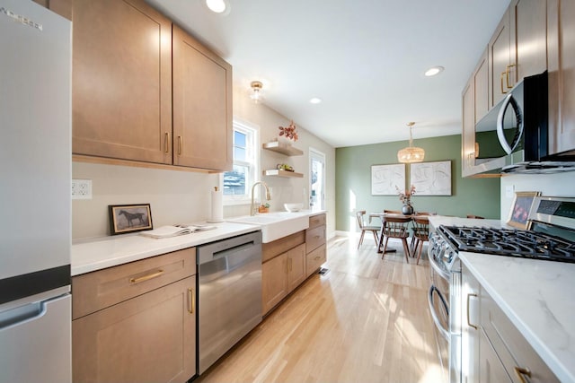 kitchen with appliances with stainless steel finishes, sink, hanging light fixtures, light hardwood / wood-style floors, and light stone countertops