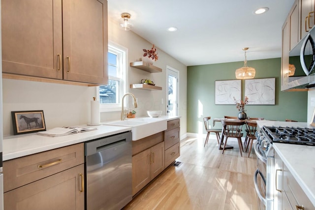 kitchen featuring pendant lighting, appliances with stainless steel finishes, sink, and light hardwood / wood-style flooring