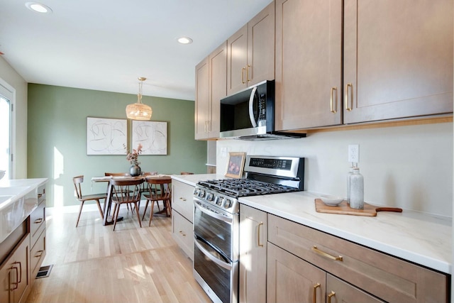 kitchen with stainless steel appliances, light stone counters, light hardwood / wood-style floors, light brown cabinetry, and decorative light fixtures