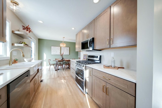 kitchen featuring stainless steel appliances, sink, pendant lighting, and light hardwood / wood-style flooring