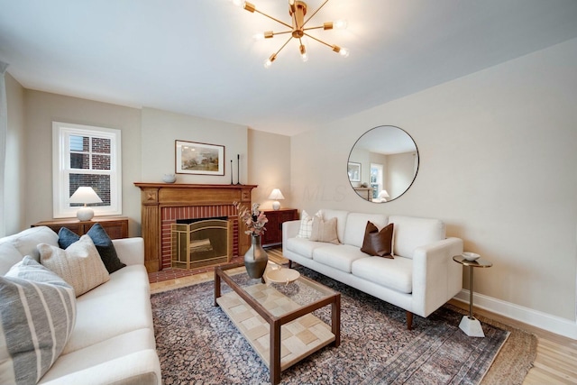 living room with an inviting chandelier, wood-type flooring, and a brick fireplace