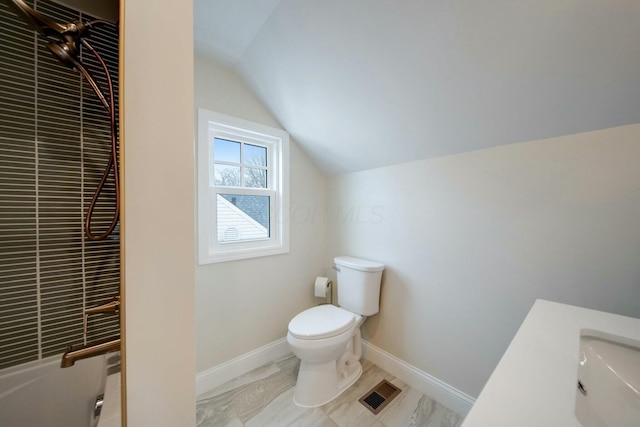 bathroom featuring sink, toilet, vaulted ceiling, and a tile shower