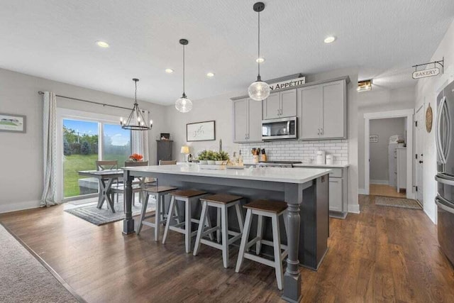 kitchen featuring decorative light fixtures, dark hardwood / wood-style flooring, backsplash, gray cabinetry, and a center island with sink