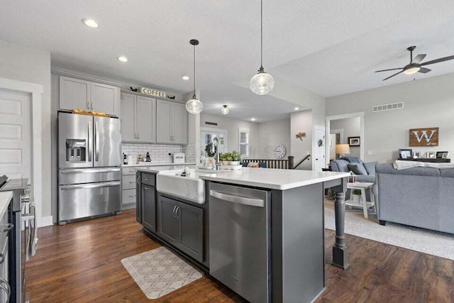 kitchen with appliances with stainless steel finishes, pendant lighting, a breakfast bar, an island with sink, and gray cabinets