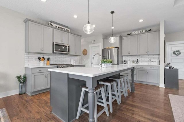 kitchen featuring pendant lighting, stainless steel appliances, a kitchen breakfast bar, gray cabinets, and a kitchen island with sink