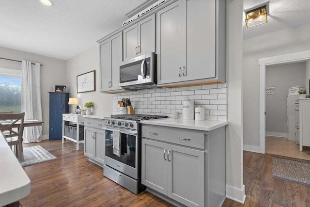 kitchen with backsplash, dark hardwood / wood-style floors, gray cabinetry, and stainless steel appliances