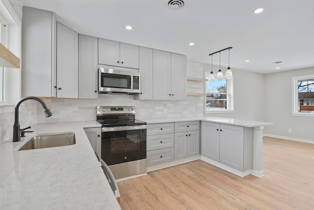 kitchen with stainless steel appliances, light hardwood / wood-style floors, sink, hanging light fixtures, and kitchen peninsula