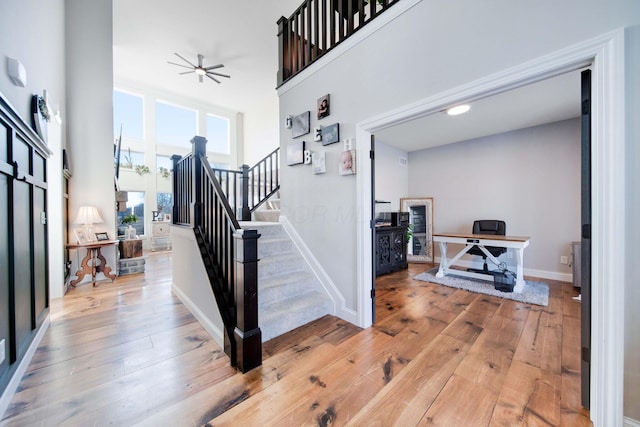 staircase with hardwood / wood-style floors, a towering ceiling, and ceiling fan