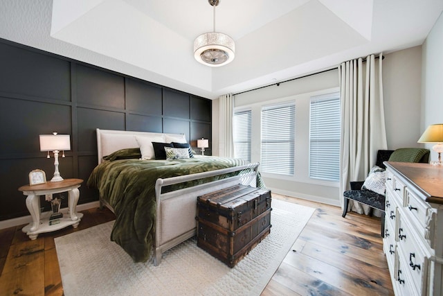 bedroom with a raised ceiling and light wood-type flooring