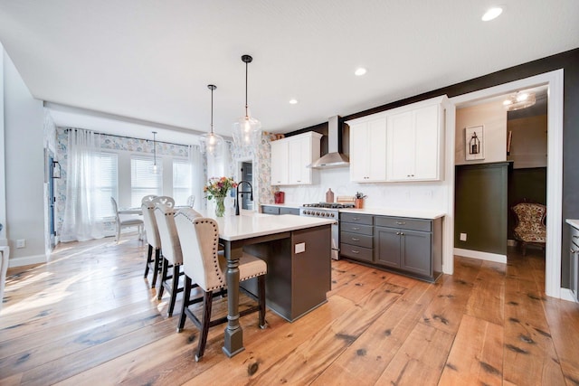 kitchen with wall chimney exhaust hood, decorative light fixtures, a center island with sink, high end stainless steel range oven, and white cabinets