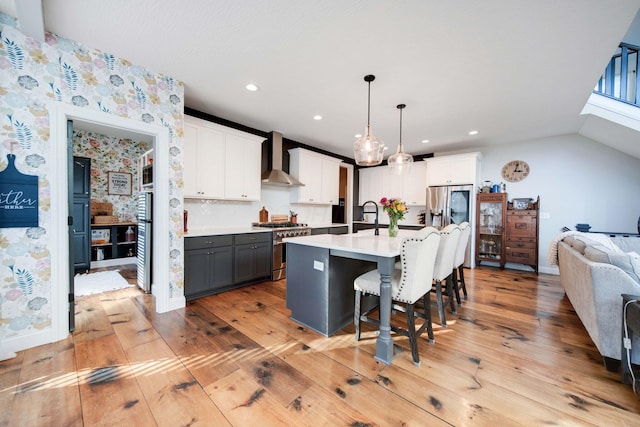 kitchen with white cabinetry, decorative light fixtures, wall chimney exhaust hood, and appliances with stainless steel finishes