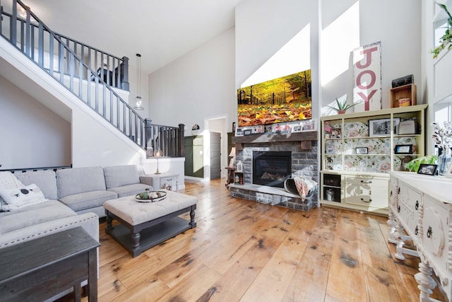 living room with wood-type flooring, a stone fireplace, and high vaulted ceiling