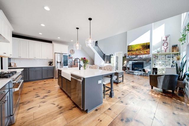 kitchen featuring sink, appliances with stainless steel finishes, white cabinetry, a kitchen island with sink, and hanging light fixtures