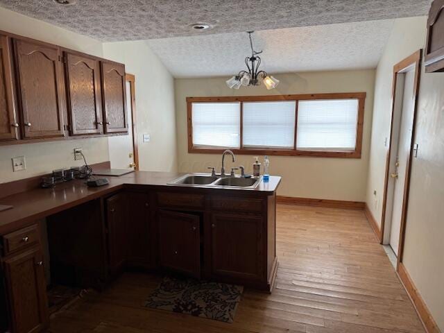 kitchen featuring kitchen peninsula, pendant lighting, sink, light wood-type flooring, and a textured ceiling