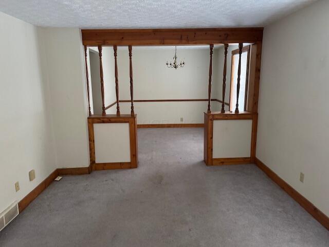 carpeted empty room featuring a textured ceiling and a chandelier