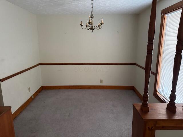 carpeted empty room with a chandelier and a textured ceiling