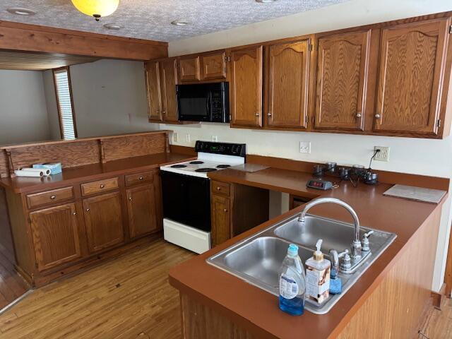 kitchen featuring a textured ceiling, white electric range, light wood-type flooring, sink, and kitchen peninsula