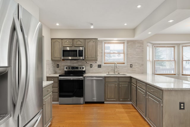 kitchen with tasteful backsplash, sink, kitchen peninsula, stainless steel appliances, and light hardwood / wood-style flooring