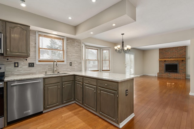 kitchen featuring sink, light stone counters, a brick fireplace, light hardwood / wood-style flooring, and appliances with stainless steel finishes