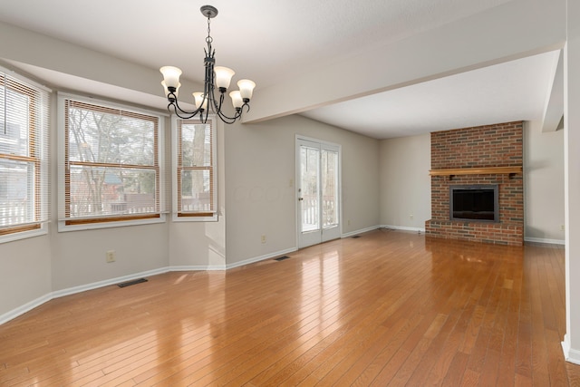 unfurnished living room featuring a fireplace, a chandelier, and light wood-type flooring