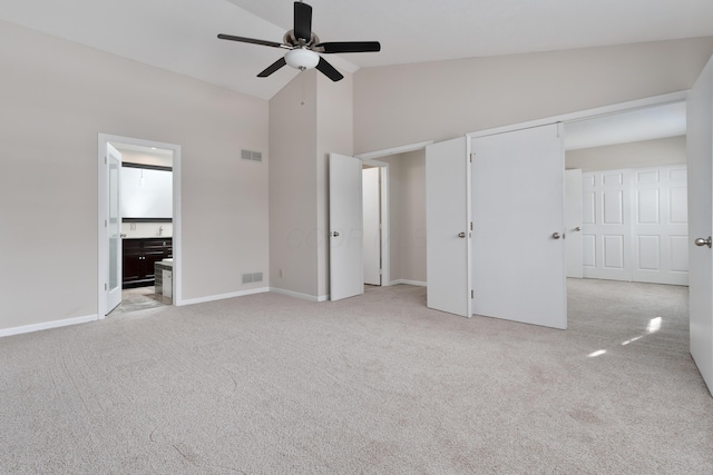 unfurnished bedroom with ensuite bathroom, high vaulted ceiling, light colored carpet, and ceiling fan