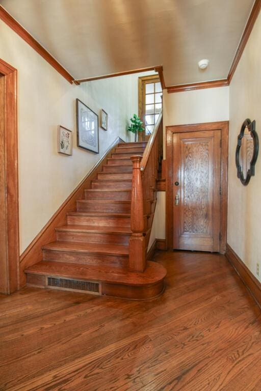 staircase with wood-type flooring and ornamental molding