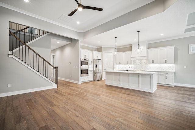 kitchen featuring pendant lighting, white cabinetry, an island with sink, stainless steel appliances, and light hardwood / wood-style flooring