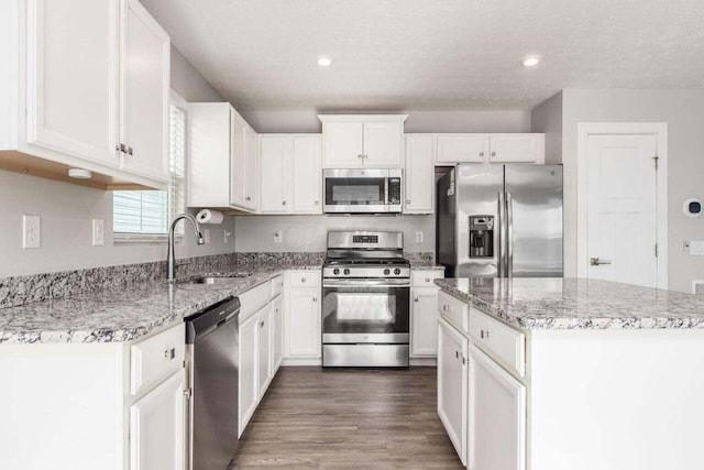 kitchen featuring light stone countertops, white cabinets, a kitchen island, stainless steel appliances, and sink