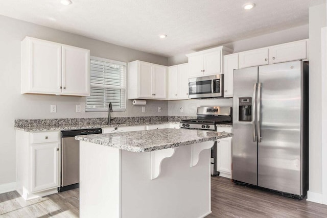 kitchen featuring appliances with stainless steel finishes, white cabinetry, light stone counters, hardwood / wood-style floors, and a center island