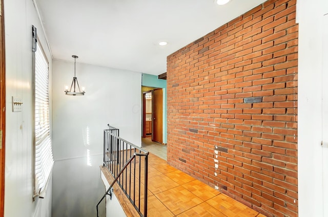 hall with a notable chandelier, light parquet flooring, and brick wall