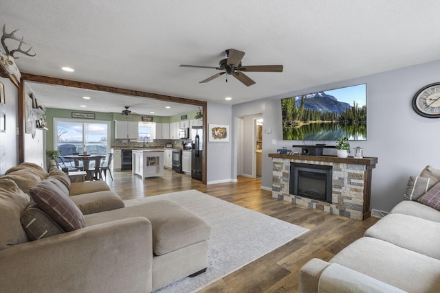 living room featuring sink, ceiling fan, hardwood / wood-style floors, beam ceiling, and a fireplace