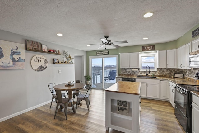 kitchen with sink, dark wood-type flooring, butcher block counters, white cabinetry, and black appliances