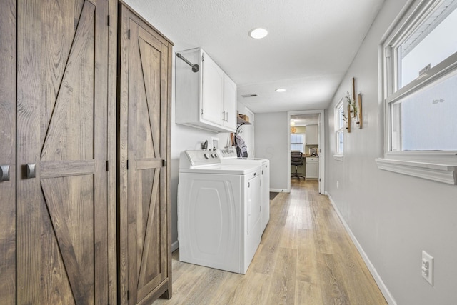 laundry area featuring cabinets, washer and clothes dryer, light hardwood / wood-style flooring, and a textured ceiling