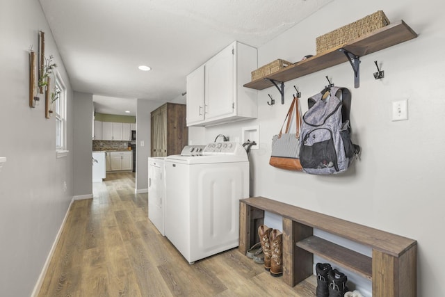 laundry room with cabinets, washing machine and dryer, light hardwood / wood-style flooring, and a textured ceiling