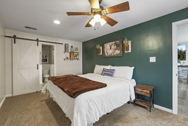 carpeted bedroom with a barn door, ceiling fan, and ensuite bathroom