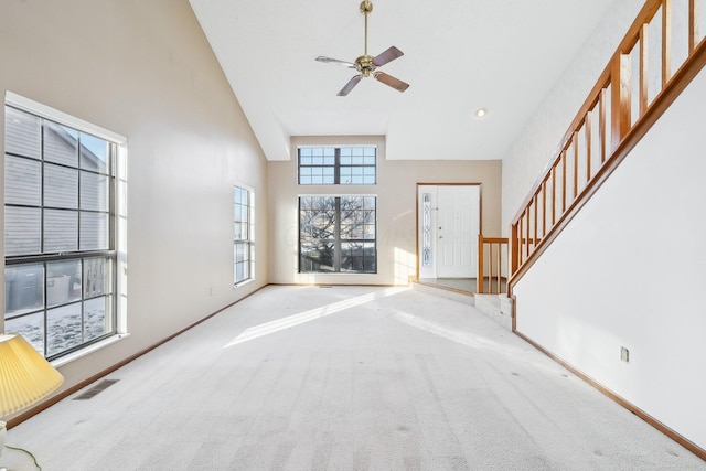 unfurnished living room with ceiling fan, light colored carpet, and a towering ceiling