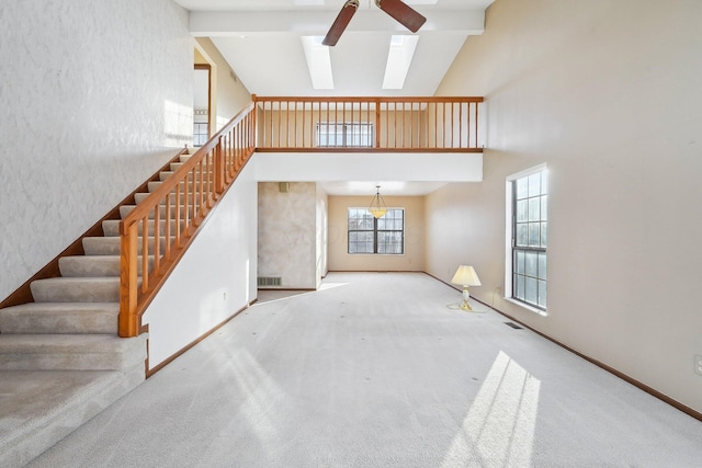 unfurnished living room with beamed ceiling, a skylight, carpet, high vaulted ceiling, and ceiling fan